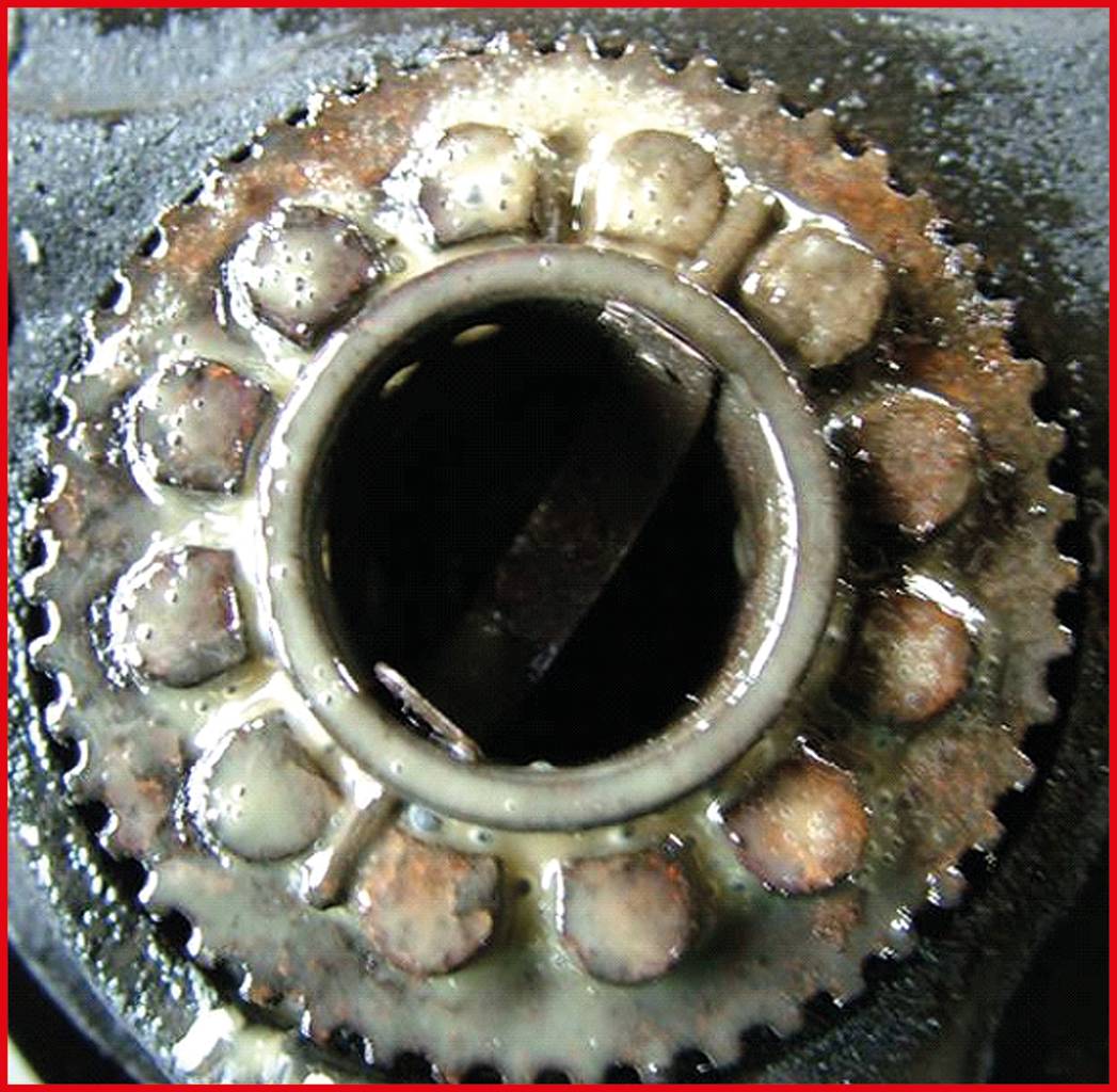 Zbliżenie zardzewiałego łożyska zębatego, pokrytego brudem i olejem. Łożysko wykazuje wyraźne oznaki zużycia.