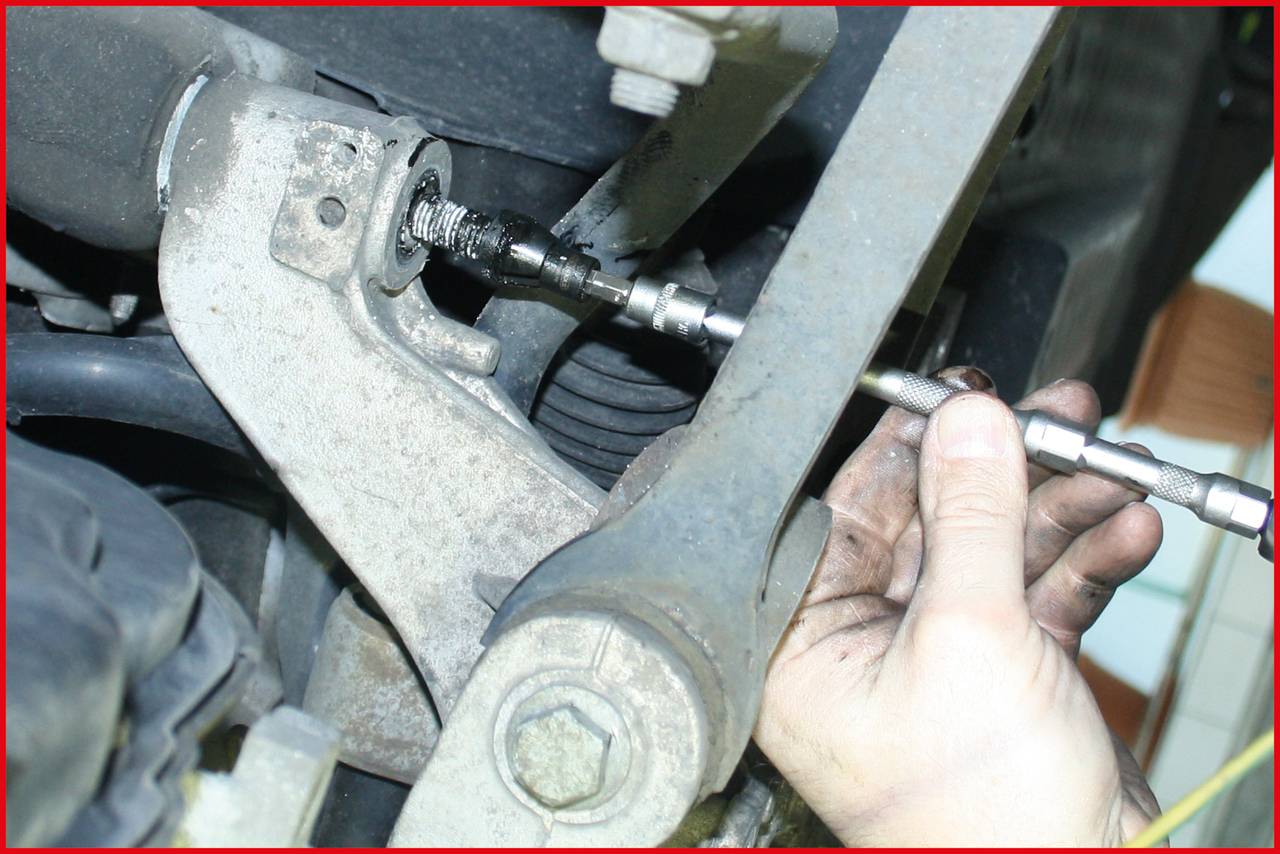 'Zbliżenie dłoni używającej narzędzia mechanicznego przy zawieszeniu pojazdu. Fokus skierowany jest na pracę naprawczą.'