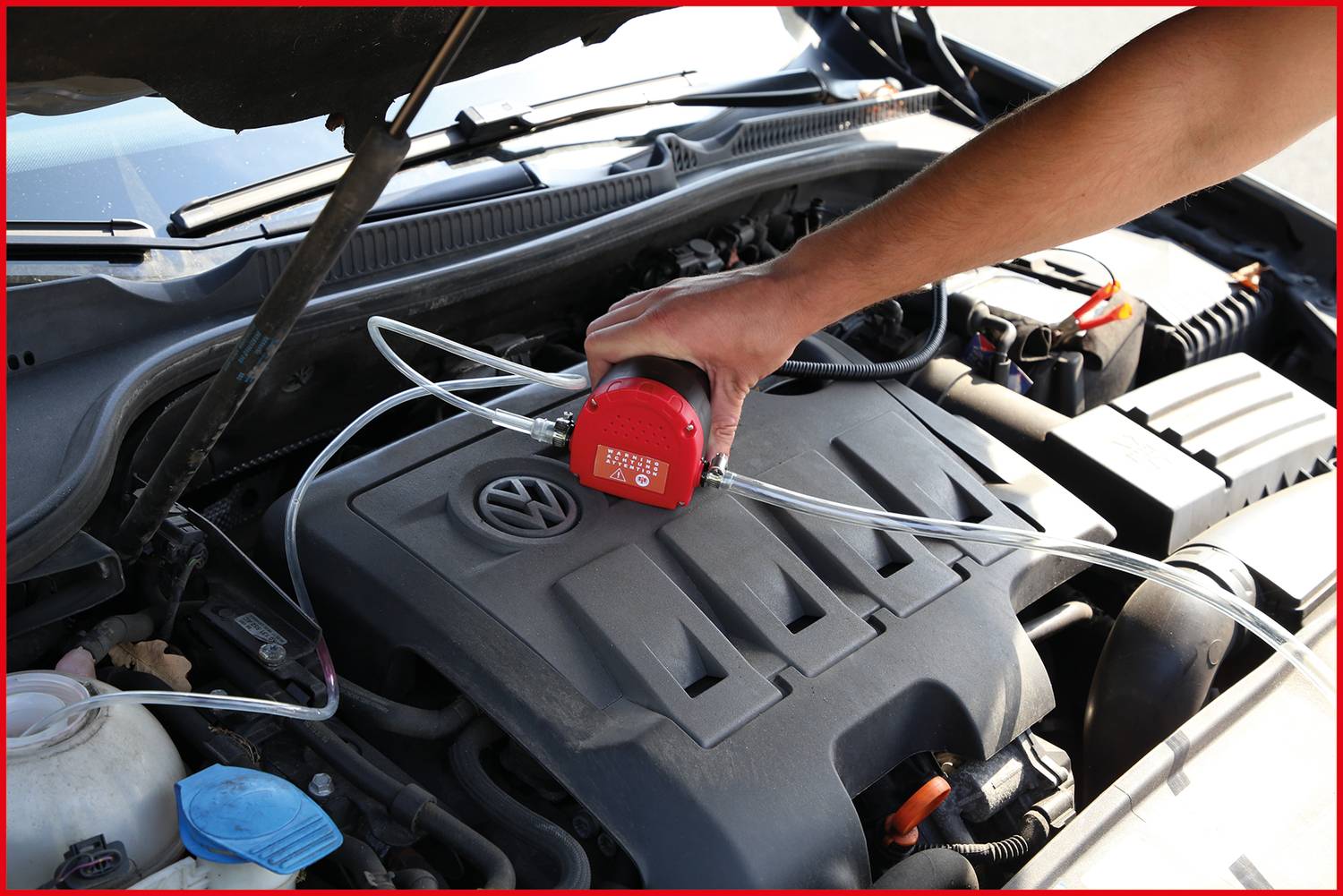 Osoba sprawdza poziom oleju w samochodzie za pomocą miernika. Maska silnika jest otwarta, widoczny jest blok silnika.
