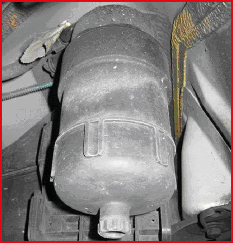 Przestarzały filtr cząstek stałych pojazdu, lekko pokryty kurzem, zamontowany pod podwoziem samochodu.