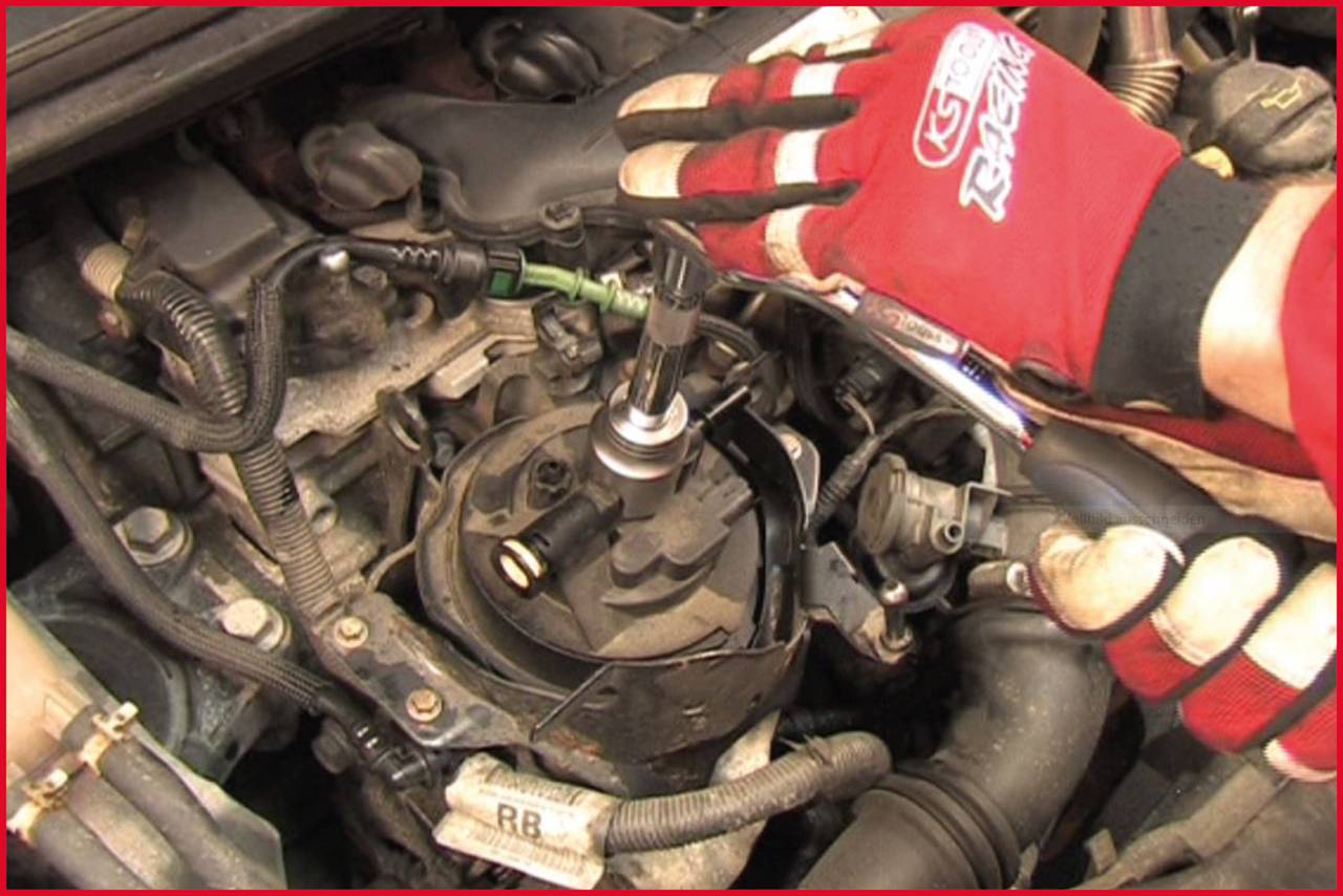 Mechanik w czerwonych rękawiczkach naprawia silnik samochodu i wyciąga świecę zapłonową z bloku silnika.