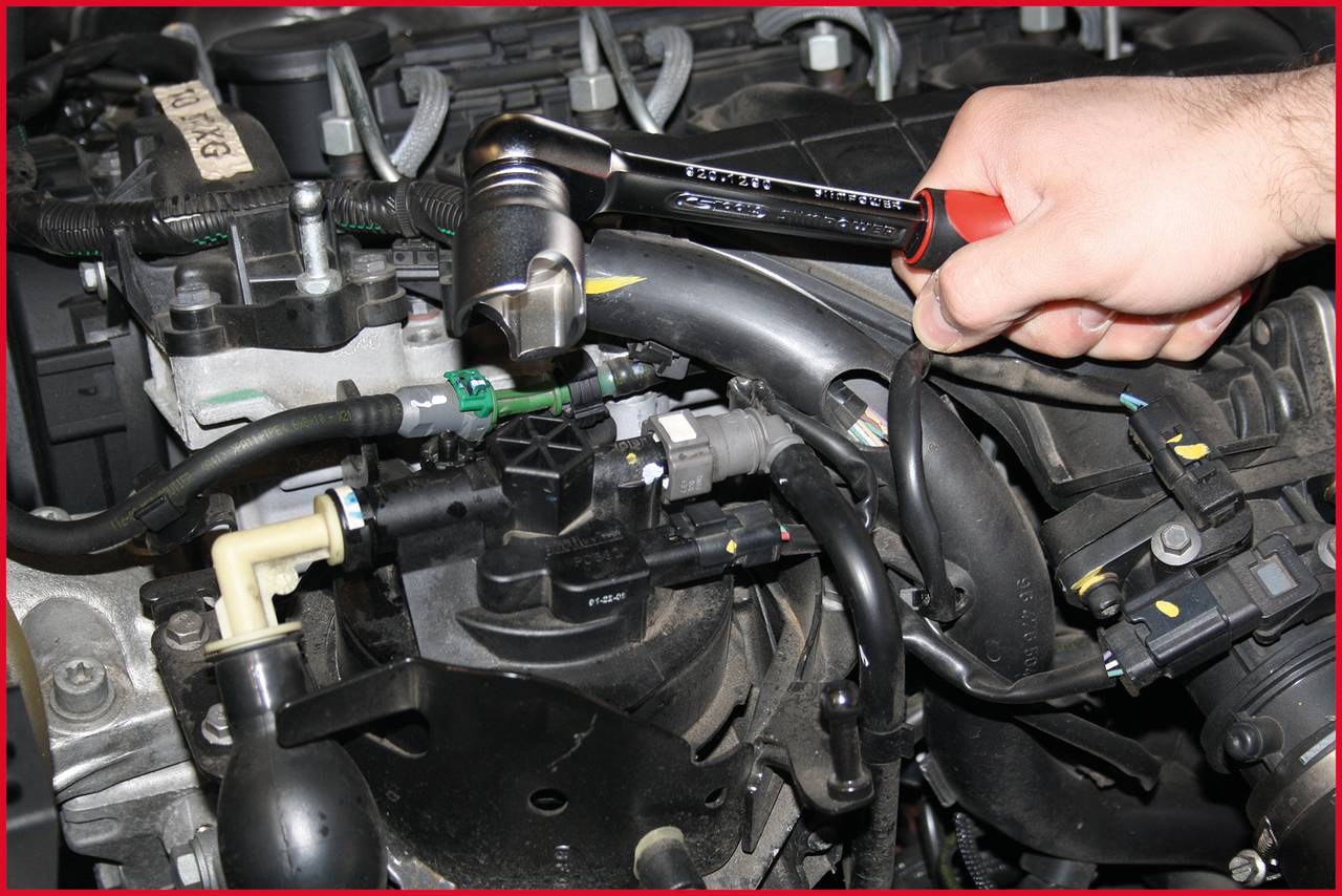 Ręka używa klucza z grzechotką na silniku. Fokus jest na konserwacji części w komorze silnika pojazdu.