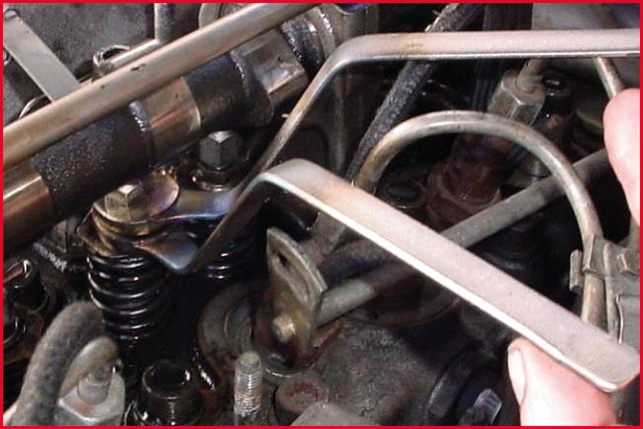 Mechanik reguluje luz zaworowy silnika za pomocą szczelinomierza. Widoczne są sprężyna, dźwignia i metalowe elementy wewnątrz silnika.