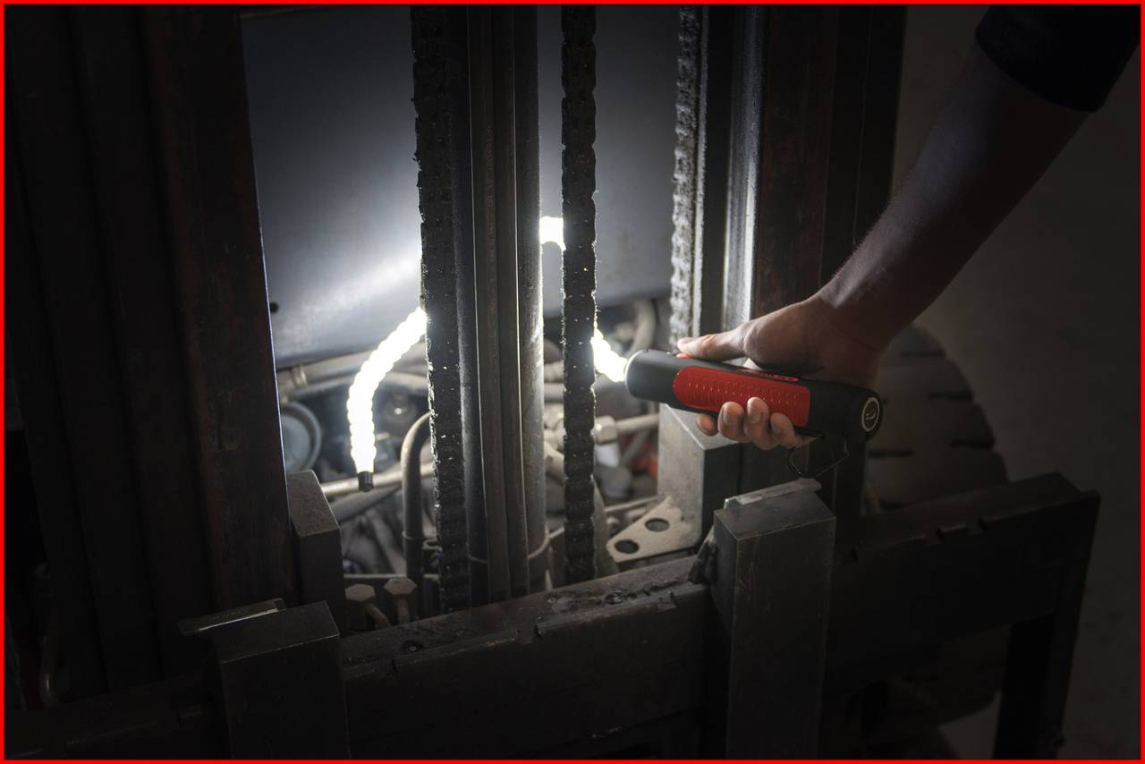 Osoba świeci latarką w mechanikę wózka widłowego, aby zbadać jego wnętrze.