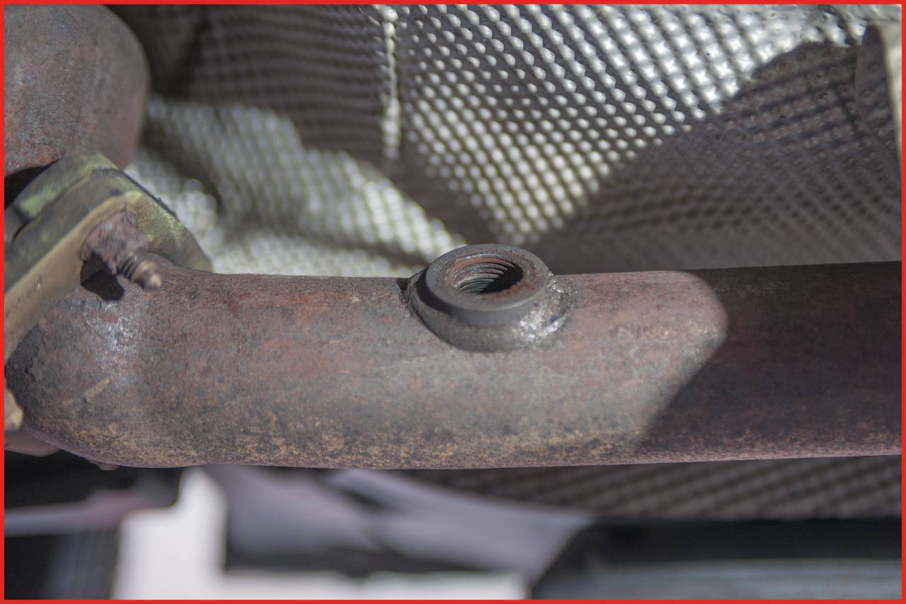 Zardzewiały przewód wydechowy z otworem gwintowanym, otoczony srebrną folią ochronną.