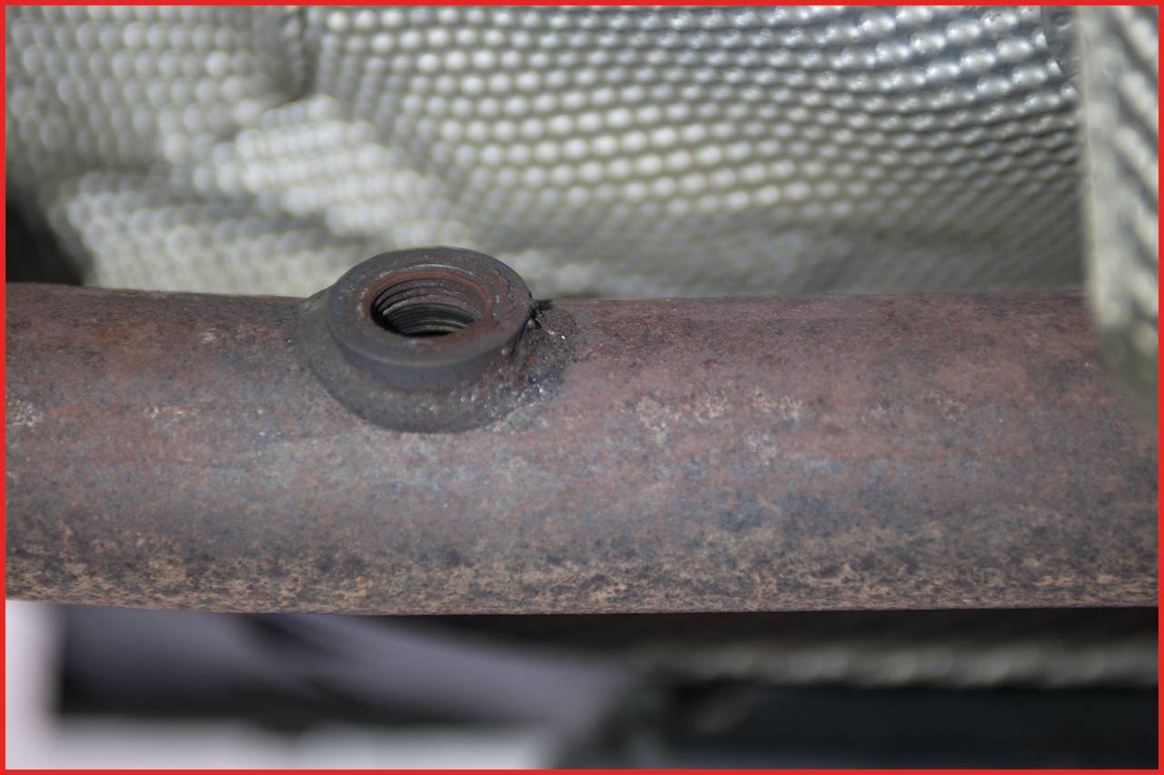 Zbliżenie zardzewiałej metalowej rury gwintowanej, otoczonej strukturą plecionego materiału.