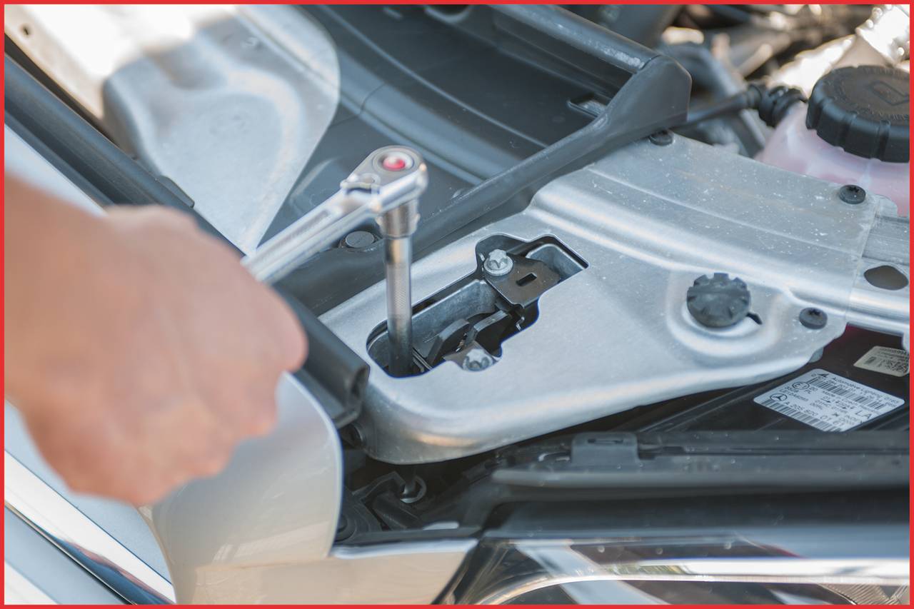 Osoba dokręca śrubę kluczem płaskim w komorze silnika samochodu. Narzędzie i części samochodowe są widoczne.
