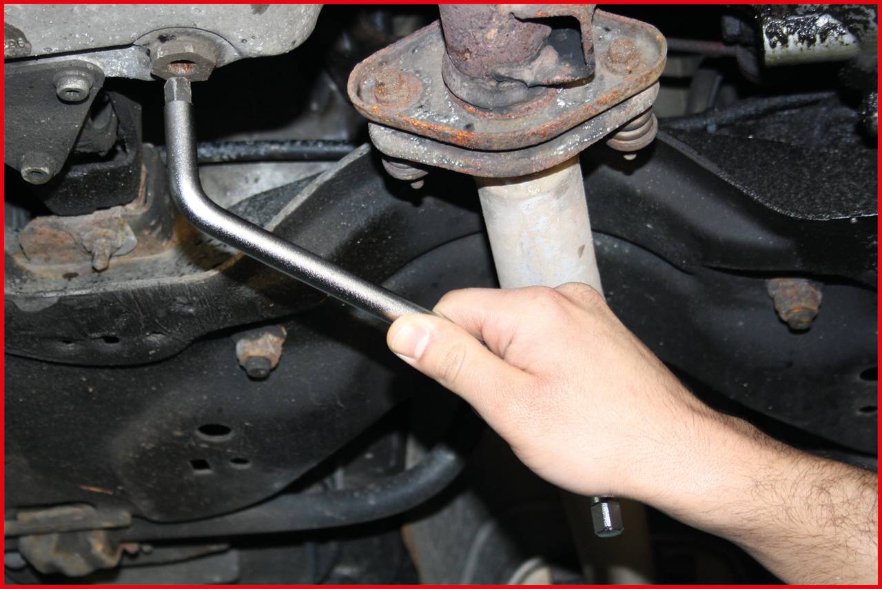 Ręka z kluczem nasadowym dokręca zardzewiałą śrubę przy elemencie samochodowym.