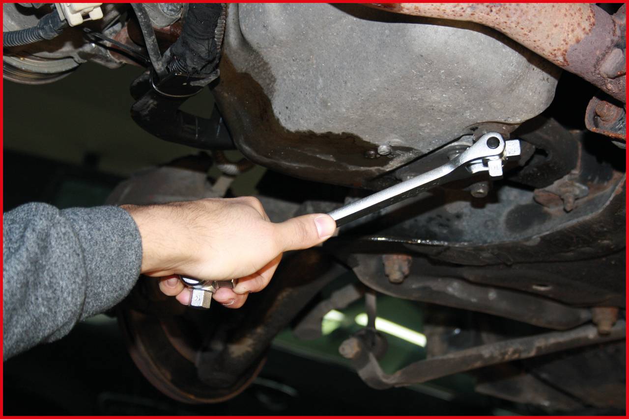 Osoba naprawia tłumik samochodu kluczem nasadowym. Leży pod pojazdem i pracuje przy układzie wydechowym.