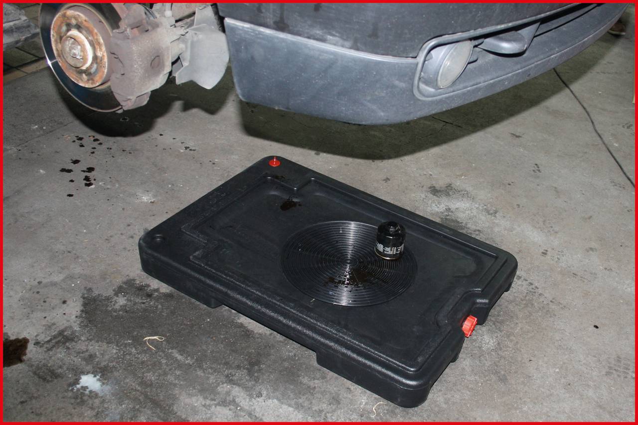 Podstawiona jest miska ociekowa pod samochodem z częściowo zdemontowanym kołem. Zbiera ona olej lub inne płyny z pojazdu.
