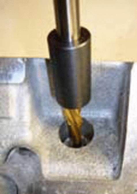 Wiertło obrabia kawałek metalu, tworząc cylindryczny otwór. Wiertło wykonane jest z mosiądzu i przedstawione jest w ruchu obrotowym.