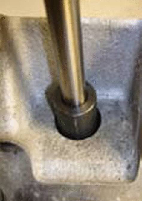 Metalowy element z pionowym cylindrycznym prętem zamontowanym w solidnej, prostokątnej podstawie.