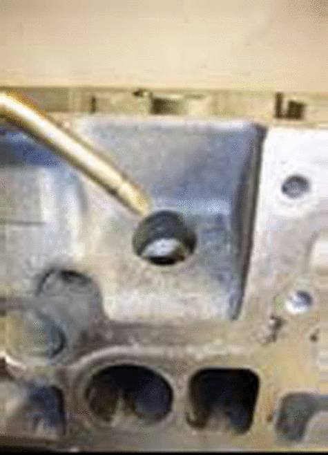 Metalowe narzędzie wskazuje na otwór w części maszyny wykonanej z szarego metalu.