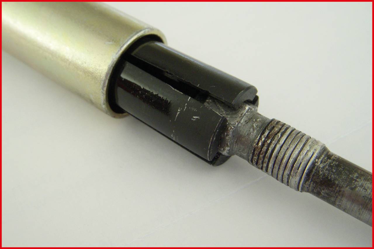 Zbliżenie metalowego elementu z czarnym tworzywem sztucznym i gwintem na końcu, prawdopodobnie część maszyny.