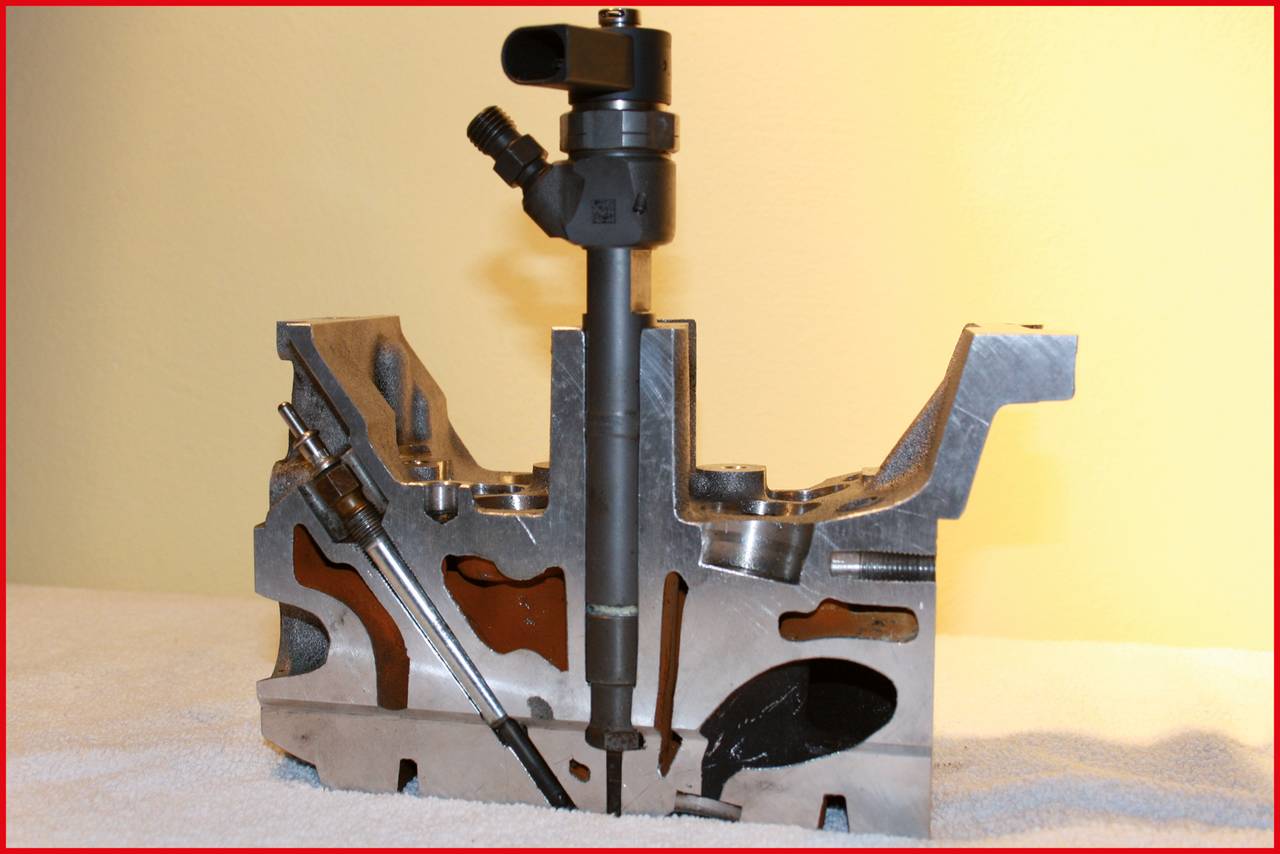 Przekrój elementu silnika ukazujący mechanizm wtryskiwacza. Metalicznie błyszcząca powierzchnia na jasnym tle.