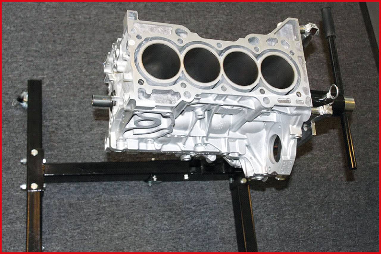 Srebrny blok silnika spoczywa na czarnym stojaku. Jest to zasadniczy element silnika spalinowego.