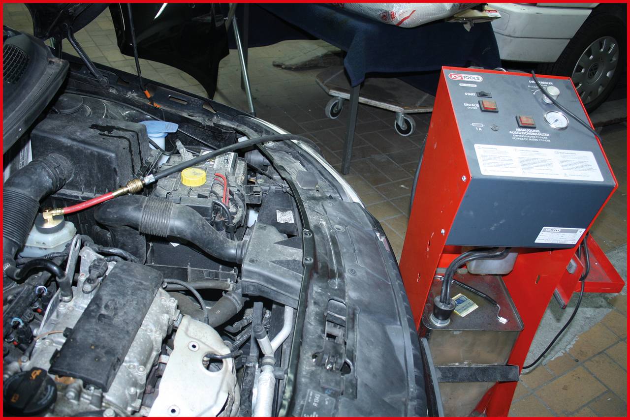 Samochód z otwartą maską w warsztacie, podłączony do czerwonego urządzenia diagnostycznego lub serwisowego.