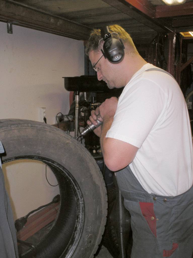 Mechanik w słuchawkach naprawia oponę samochodu w warsztacie.