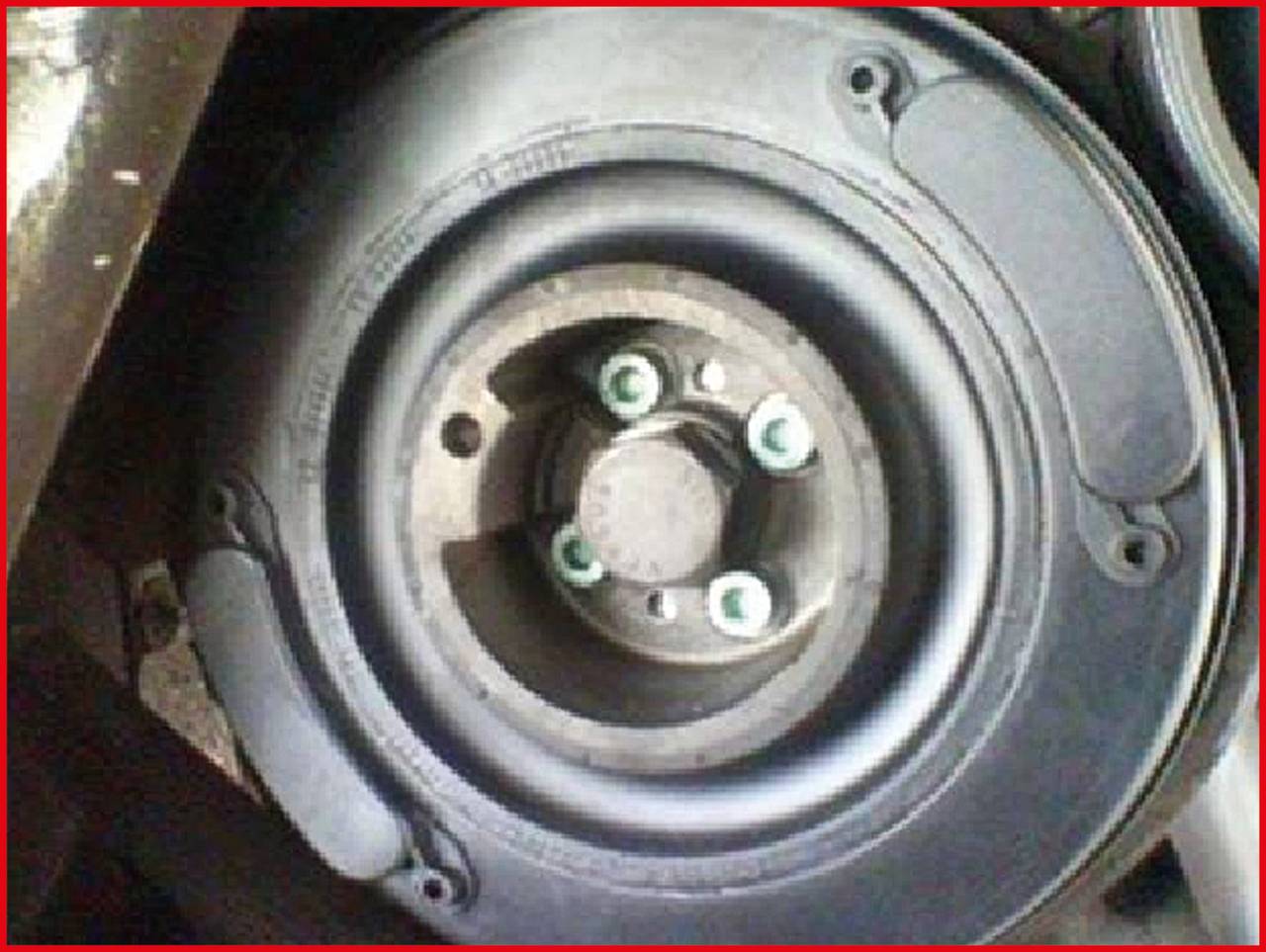 Koło zapasowe w pojeździe, z widocznymi pięcioma otworami na śruby. Koło jest zamontowane w uchwycie i wygląda na nieużywane.