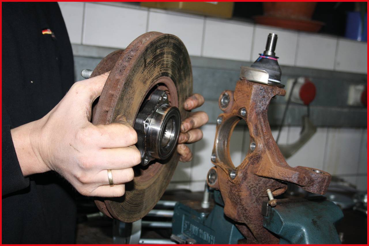 Osoba naprawia układ hamulcowy samochodu. Trzyma tarczę i piastę hamulcową, aby je zmontować. W tle widać warsztat.