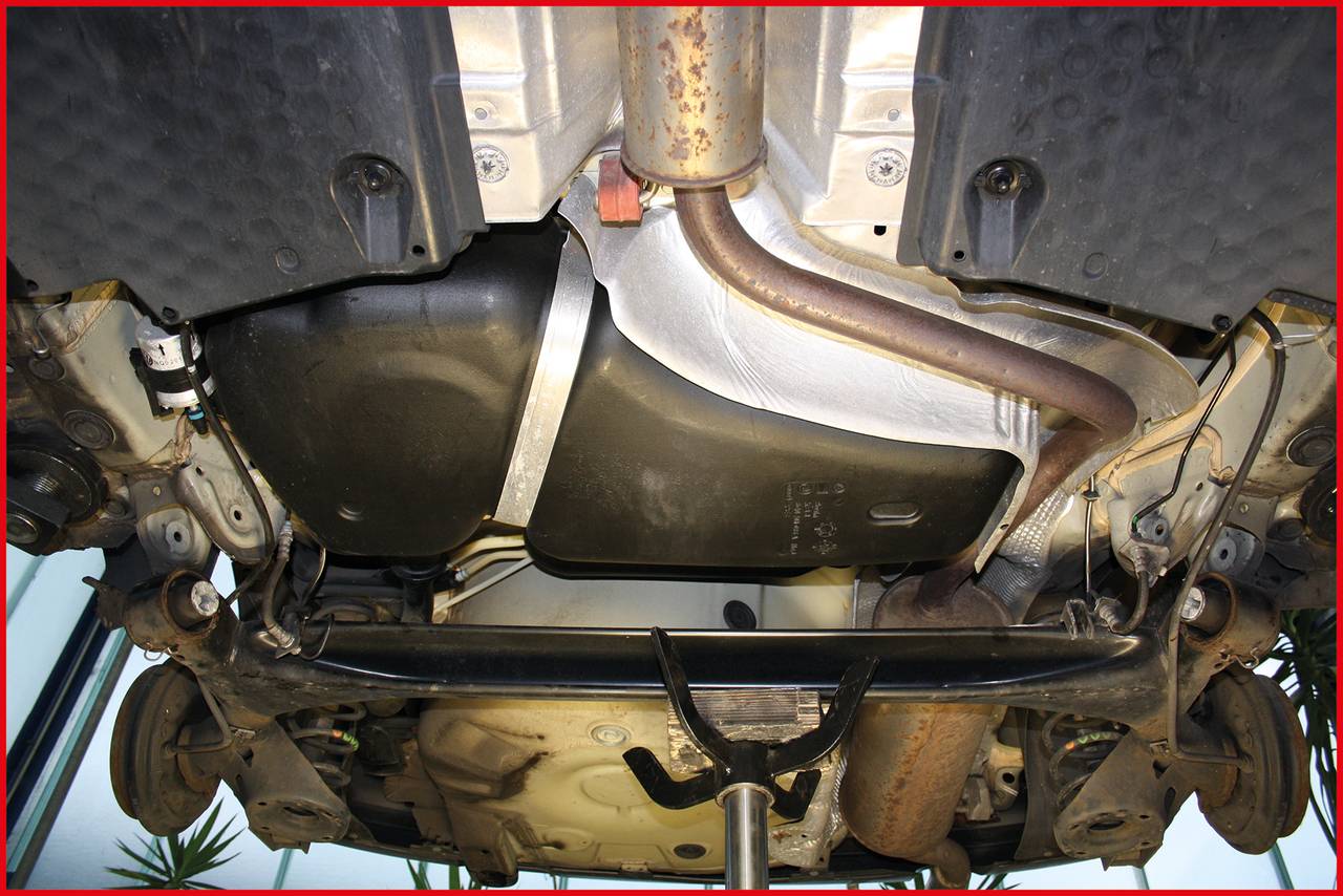 Widok od spodu samochodu z widocznym układem wydechowym i zbiornikiem paliwa, umieszczonego na podnośniku warsztatowym.