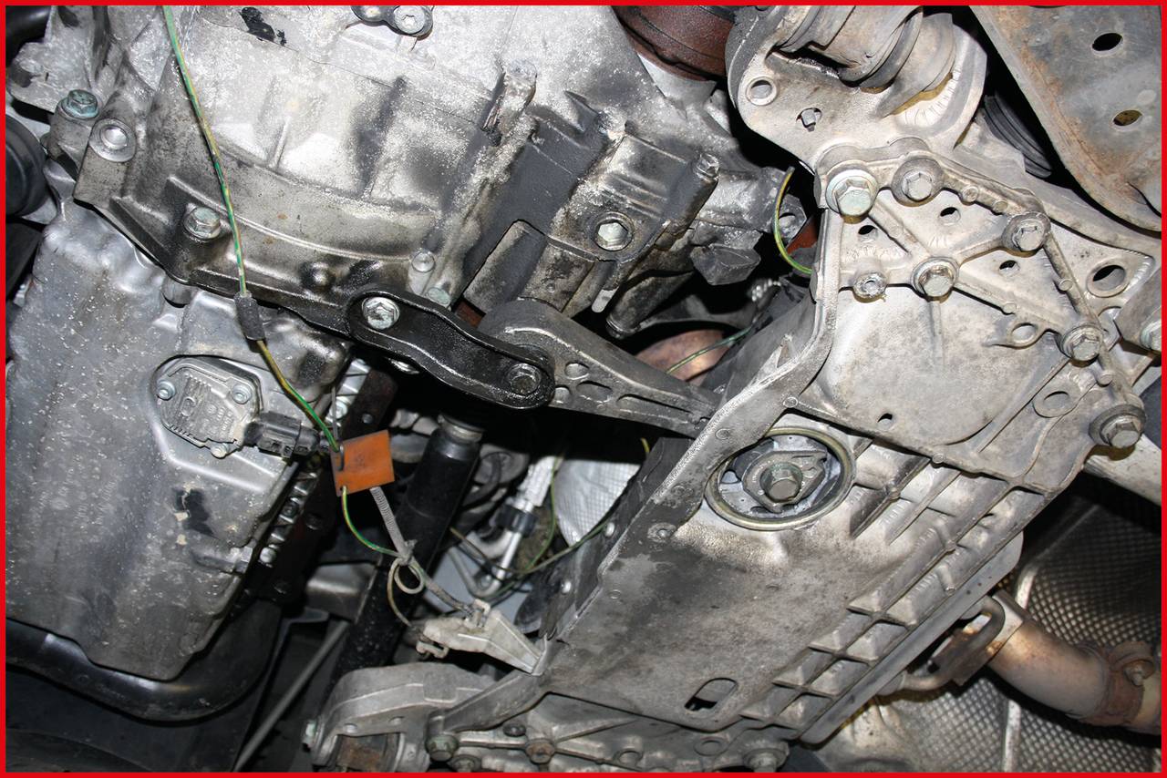 Zbliżenie mechanizmu skrzyni biegów pojazdu, ukazujące metalowe komponenty i okablowanie.