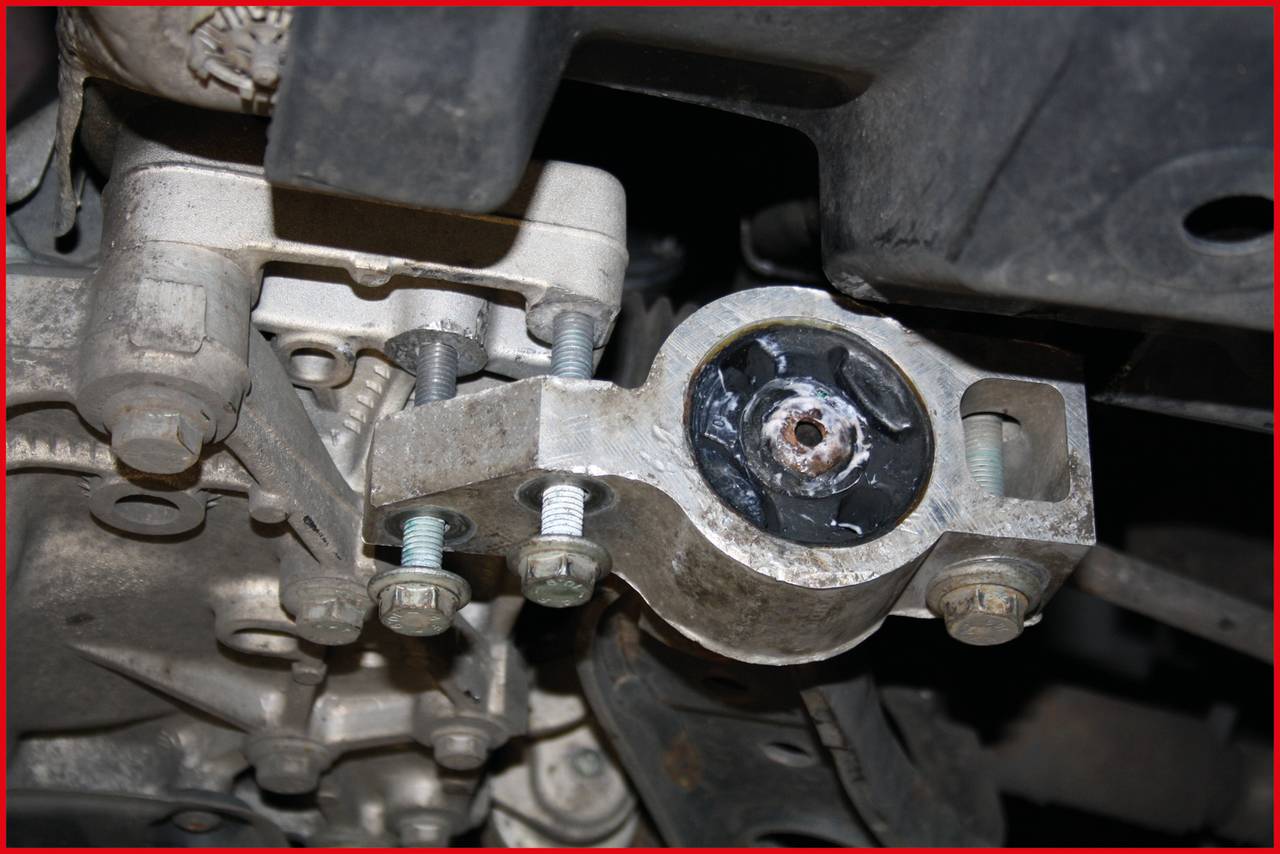 Zbliżenie mocowania silnika w samochodzie. Mocowanie jest przymocowane wieloma śrubami i wykazuje oznaki zużycia.