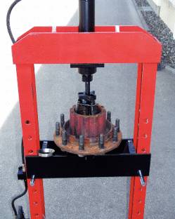 Urządzenie prasy hydraulicznej, które ściska metalowy element w centrum. Czerwone ramy i szare tło w tle.