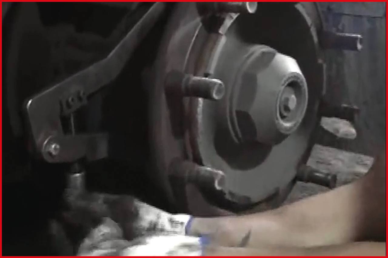 Mechanik naprawia tarczę hamulcową pojazdu, używając klucza do dokręcenia. Jego ręce są brudne od oleju.