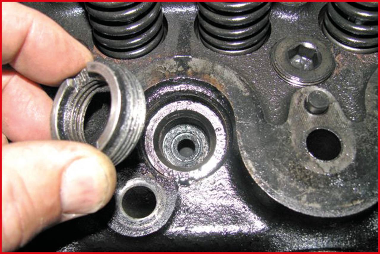 Osoba trzyma uszkodzoną tulejkę gwintowaną przed czarnym elementem maszyny. Widoczne są spiralne żeberka i sąsiednie śruby.