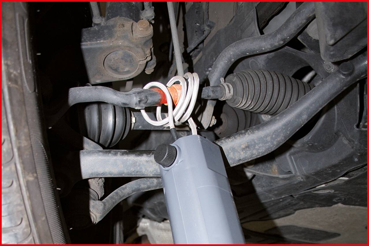 Widok zawieszenia samochodowego z amortyzatorem i układem kierowniczym. Widoczne są elementy takie jak osłony, przeguby oraz układ hydrauliczny.