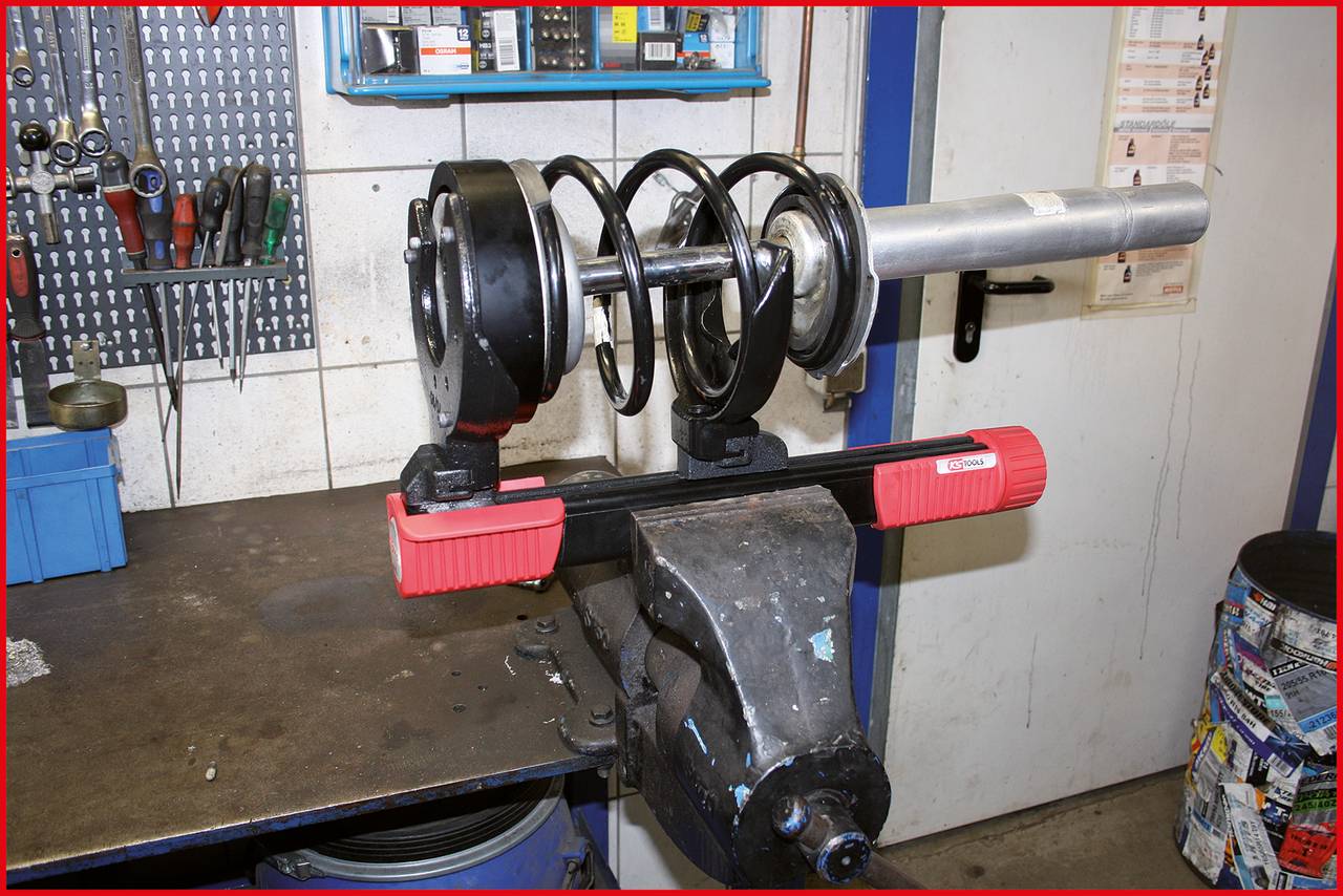 Urządzenie sprężynowe na stole warsztatowym w warsztacie samochodowym, otoczone narzędziami i częściami samochodowymi.