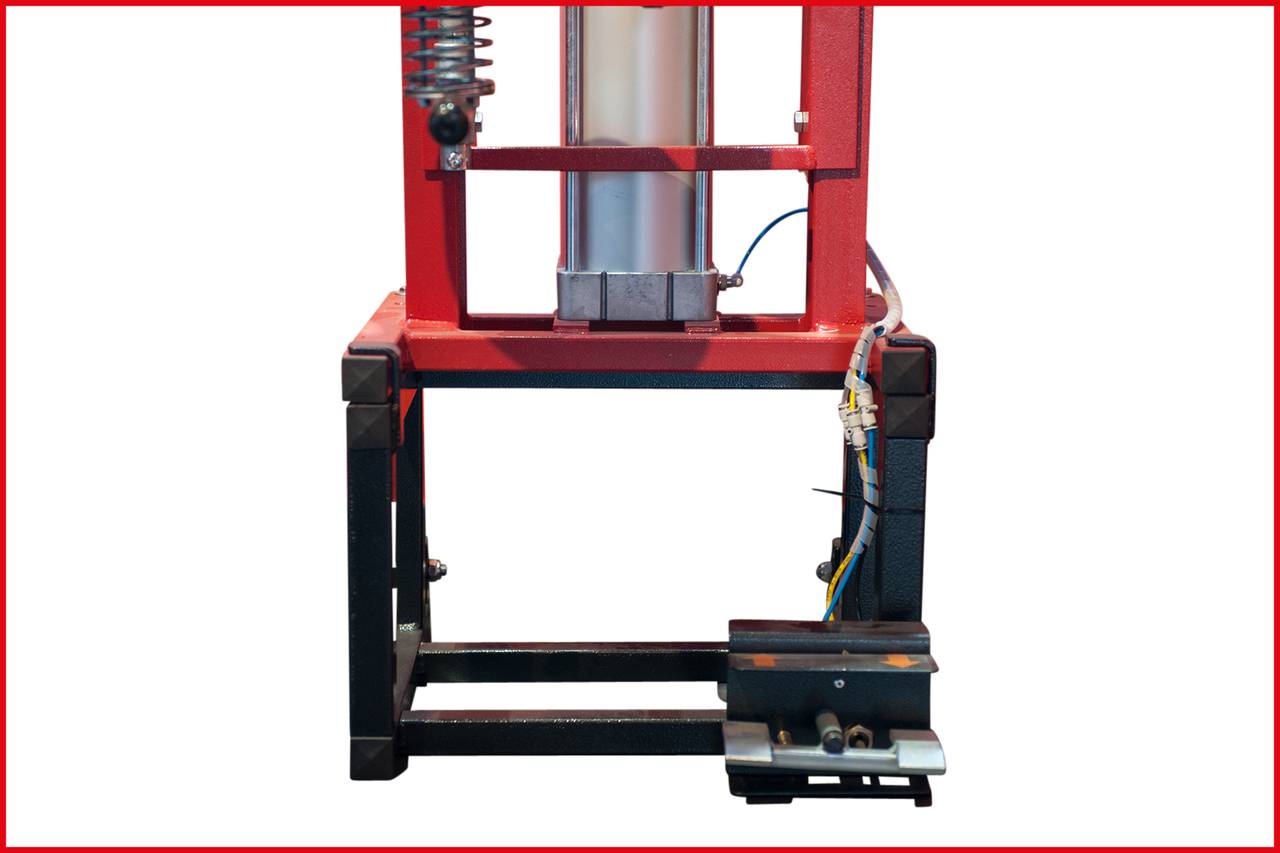 Maszyna z czerwoną ramą i srebrnym cylindrem, zamontowana na czarnej podstawie. Widoczne kable i sprężyny. Funkcja nieznana.