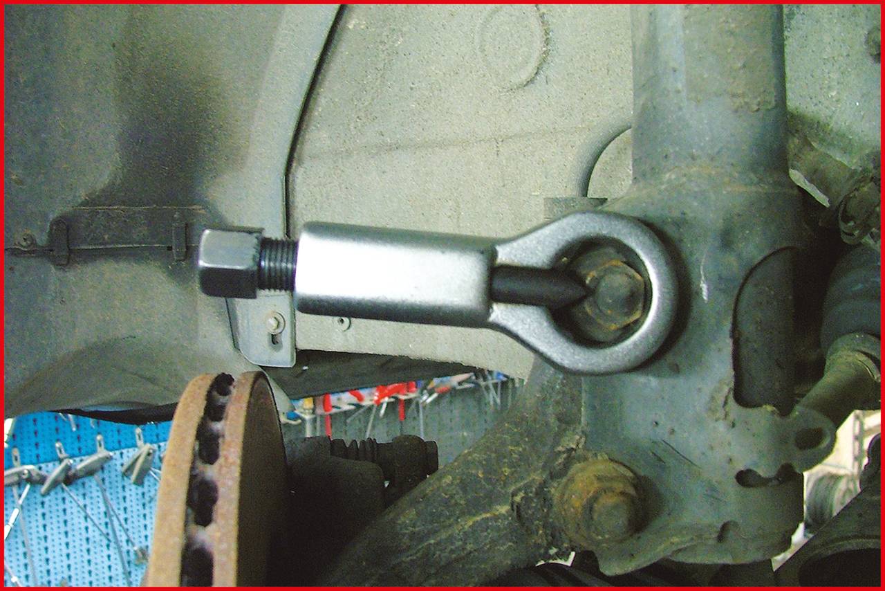 Metalowy amortyzator częściowo rozebrany, przymocowany kluczem do tylnej osi samochodu.