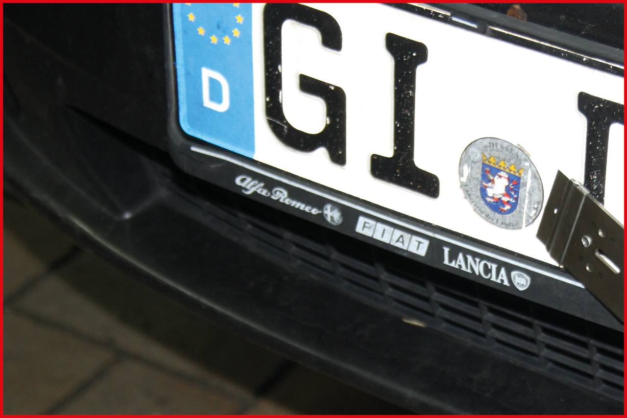 Polska tablica rejestracyjna z emblematem UE i herbem kraju. Logo marek 'Alfa Romeo', 'Fiat', 'Lancia' pod numerem rejestracyjnym.