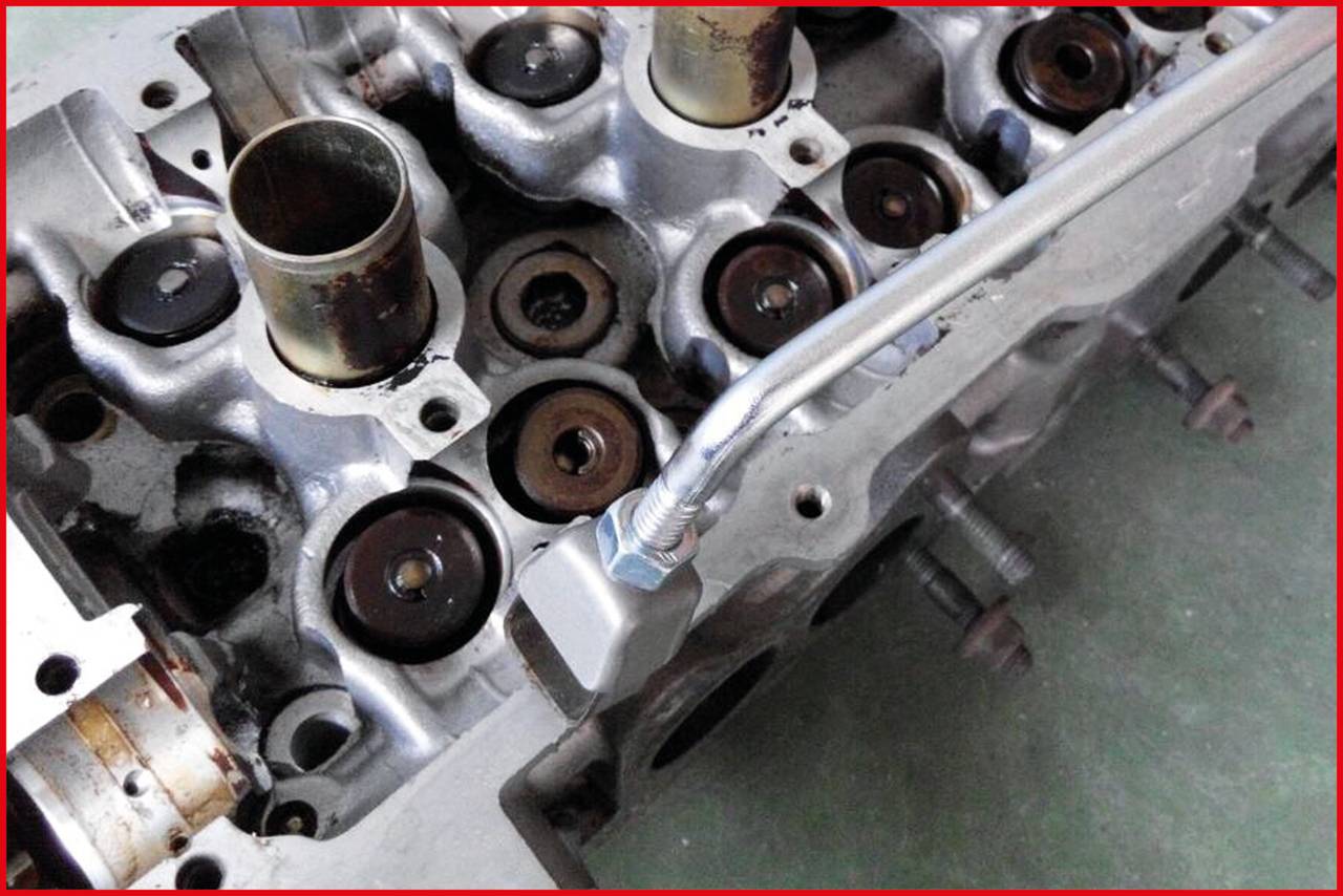 Blok silnika z widocznymi gniazdami zaworów i kanałami olejowymi. Metalowa przewodka jest zamocowana z przodu. Mechaniczny element samochodowy.