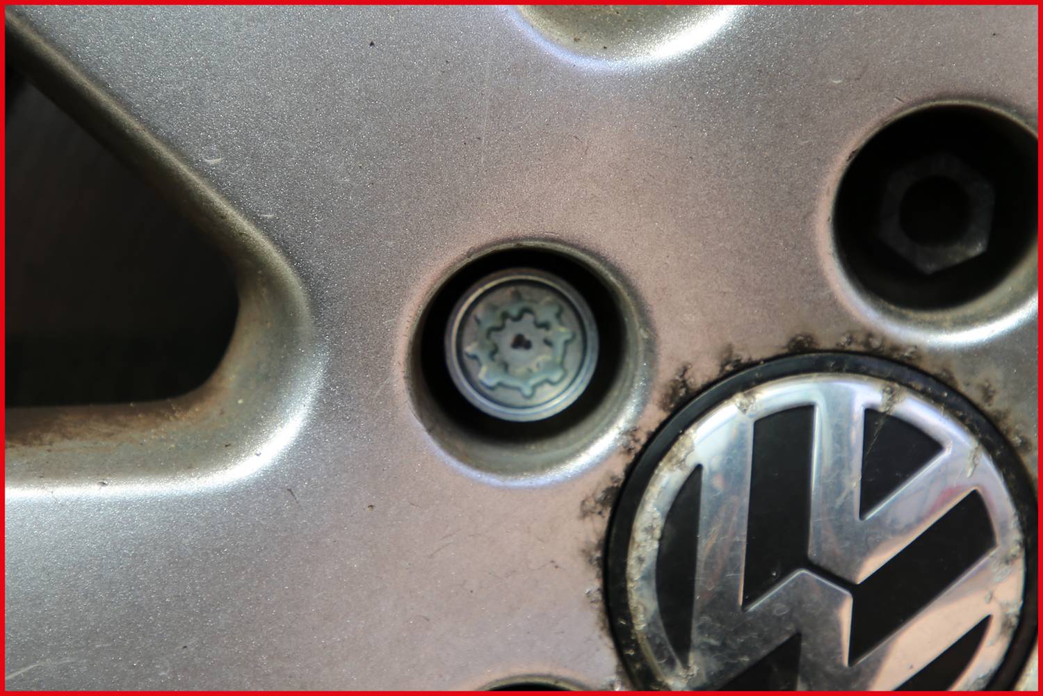 Koło samochodu z zamkiem przeciwkradzieżowym i logo marki częściowo pokrytym brudem.