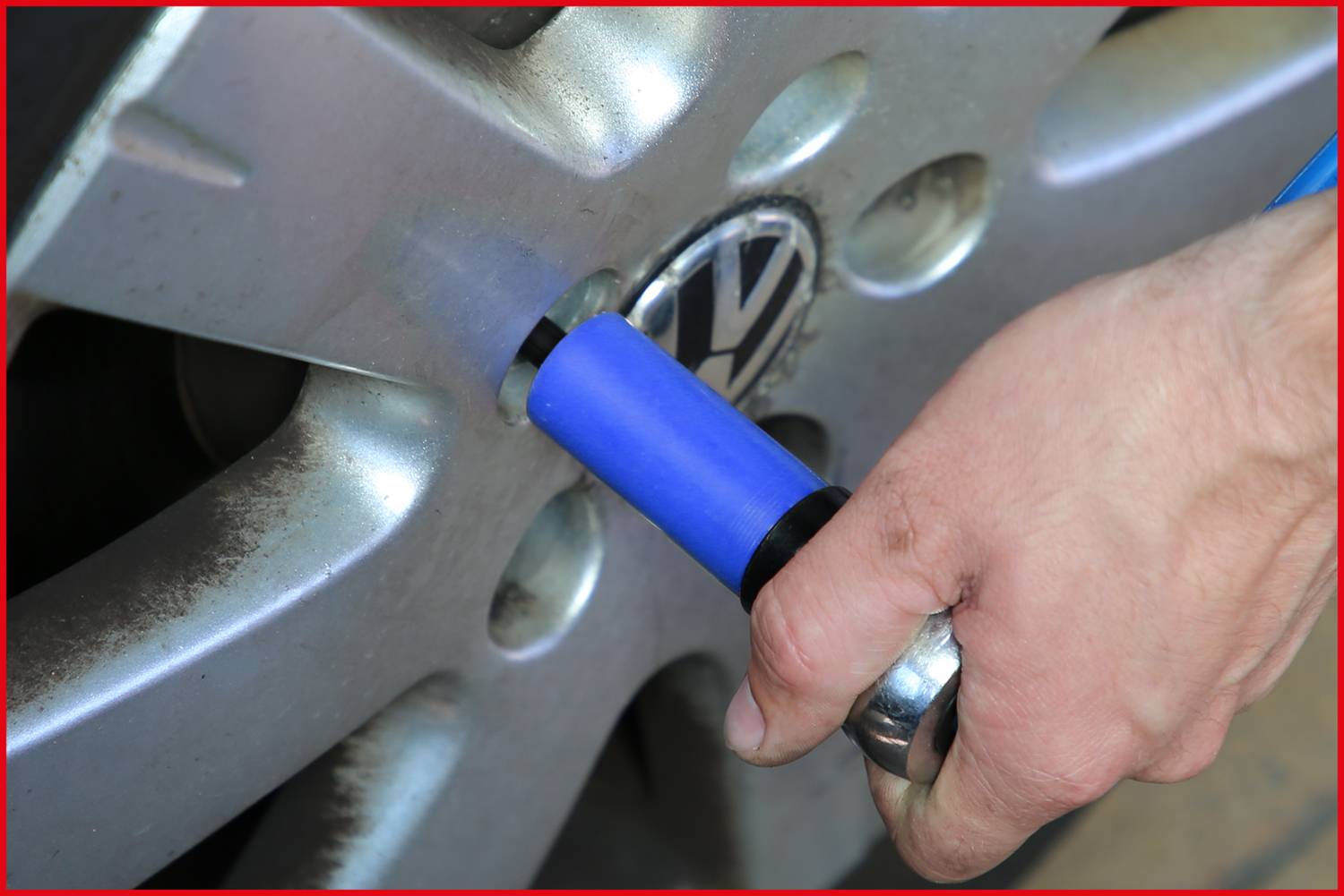 Jedna ręka trzyma narzędzie przykładane do nakrętki koła samochodu, prawdopodobnie w celu jej dokręcenia lub odkręcenia.