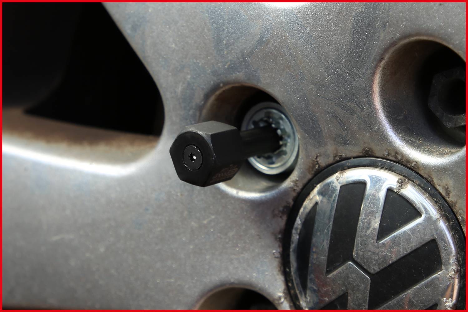 Zbliżenie zamka zabezpieczającego na srebrnym felgowym kole Volkswagena, prezentujące narzędzie bezpieczeństwa chroniące przed kradzieżą.