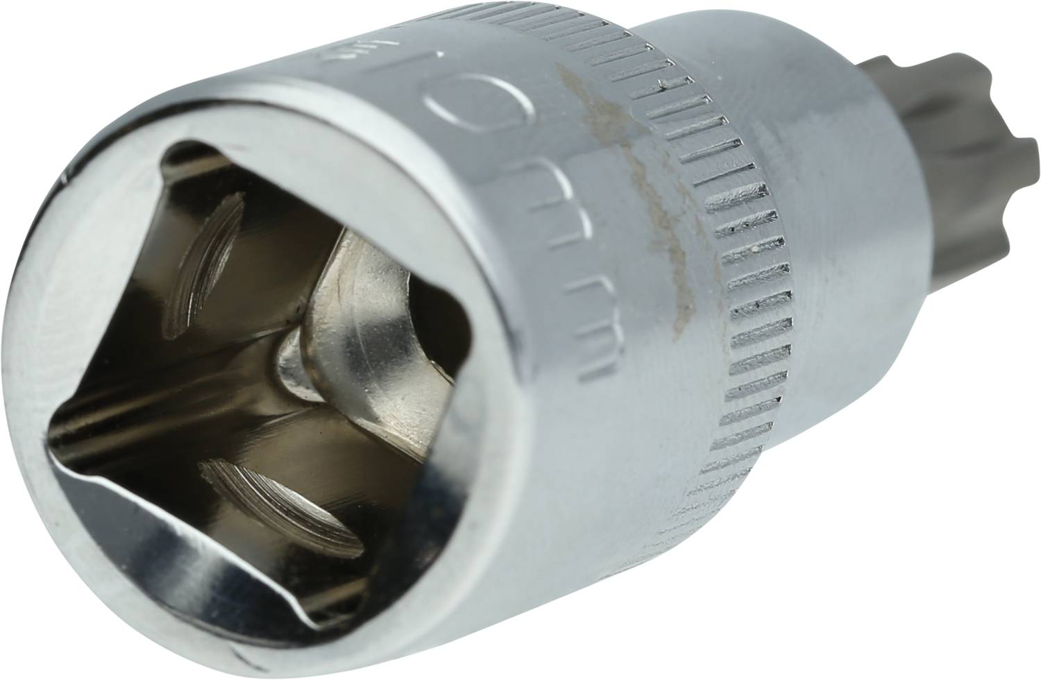 Srebrna nasadka klucza z żłobionym brzegiem i sześciokątnym otworem leży na białej powierzchni.