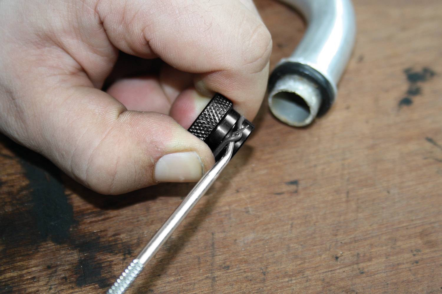 Ręka trzyma klucz nastawny, który jest dopasowywany do metalowego złącza śrubowego na surface roboczej.