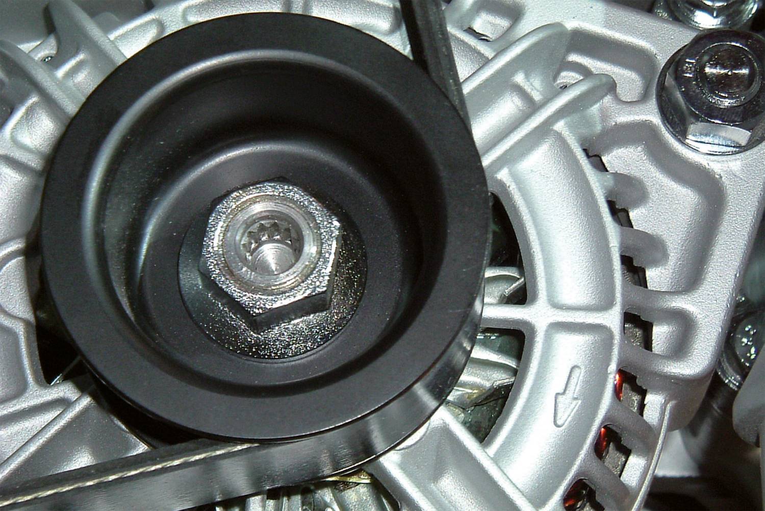 Zbliżenie alternatora samochodowego, ze szczególnym uwzględnieniem rolki napinającej i paska rozrządu. Widoczne są metalowe elementy konstrukcyjne i śruby.