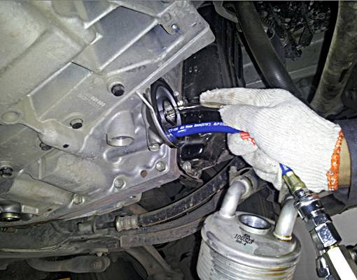 Mechanik naprawia dolną część silnika, ręka w rękawicy trzyma narzędzie. Na pierwszym planie widoczne są rury.