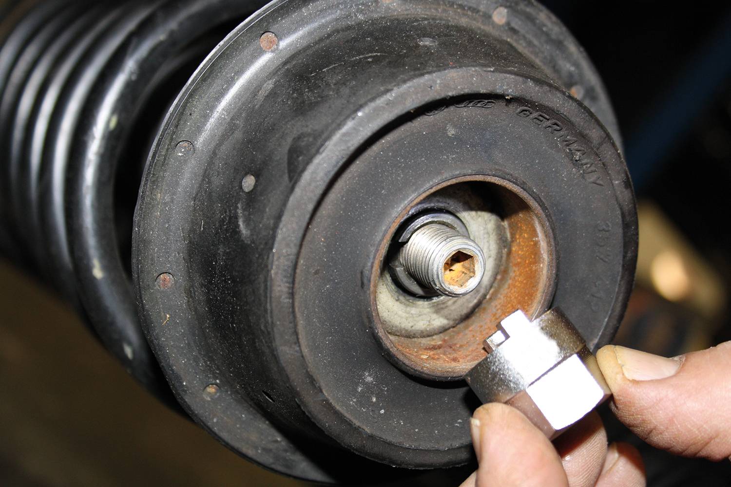 Zbliżenie na element samochodu przedstawiające mocowanie amortyzatora, z osobą trzymającą specjalistyczne narzędzie do naprawy.