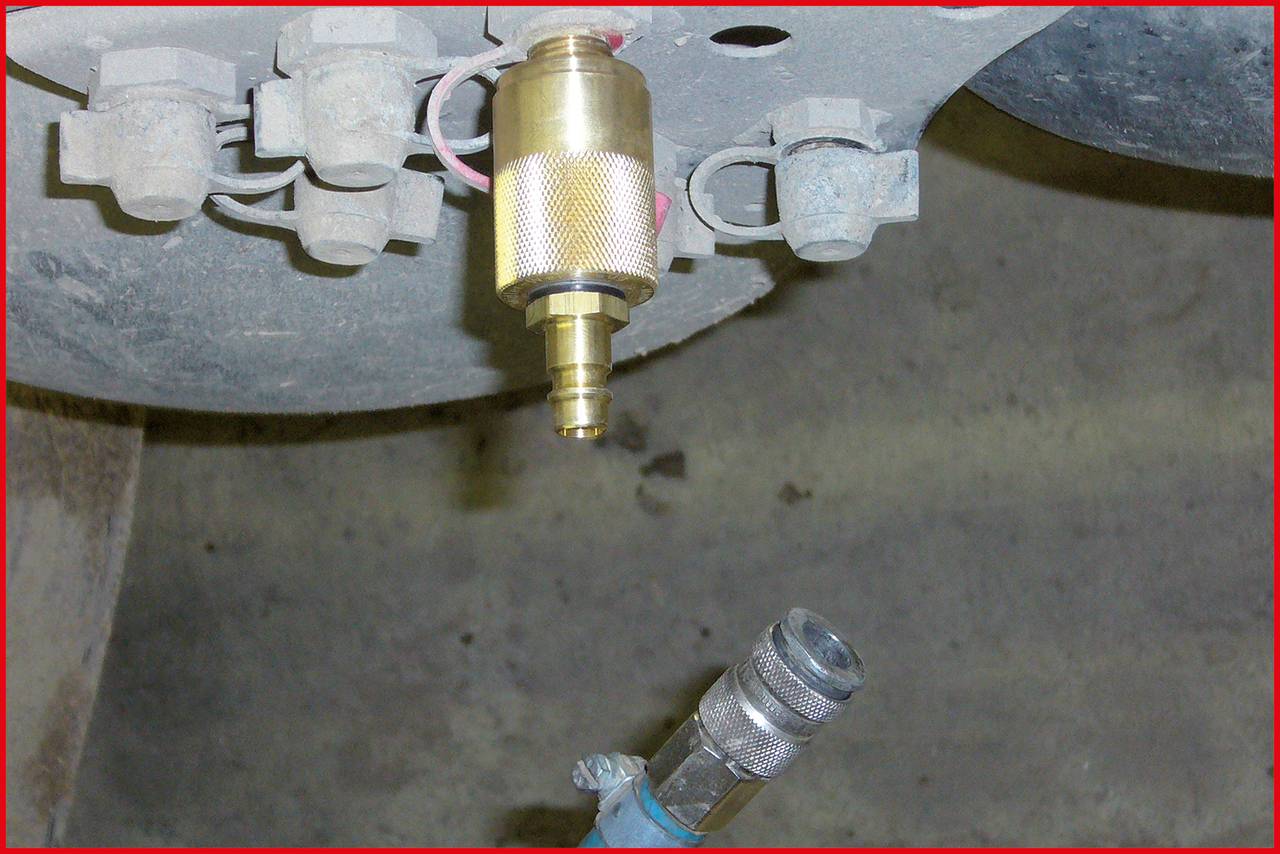 Przyrząd pomiarowy jest podłączony do zaworu opony, aby sprawdzić ciśnienie powietrza. W tle widoczne są części pojazdu.