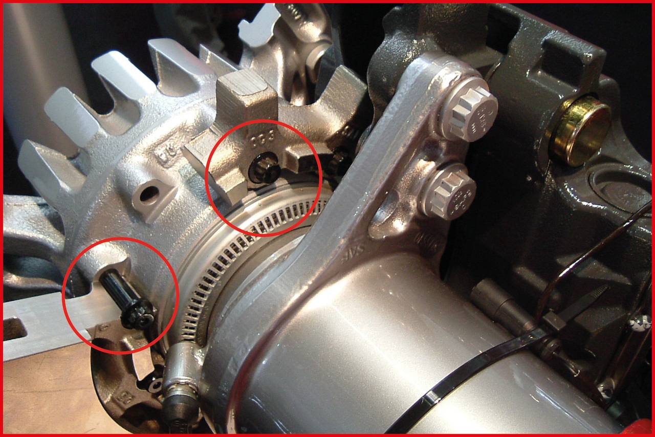 Zbliżenie mechanicznego elementu z widocznymi śrubami i kołami zębatymi. Dwa obszary zostały oznaczone czerwonymi kołami.