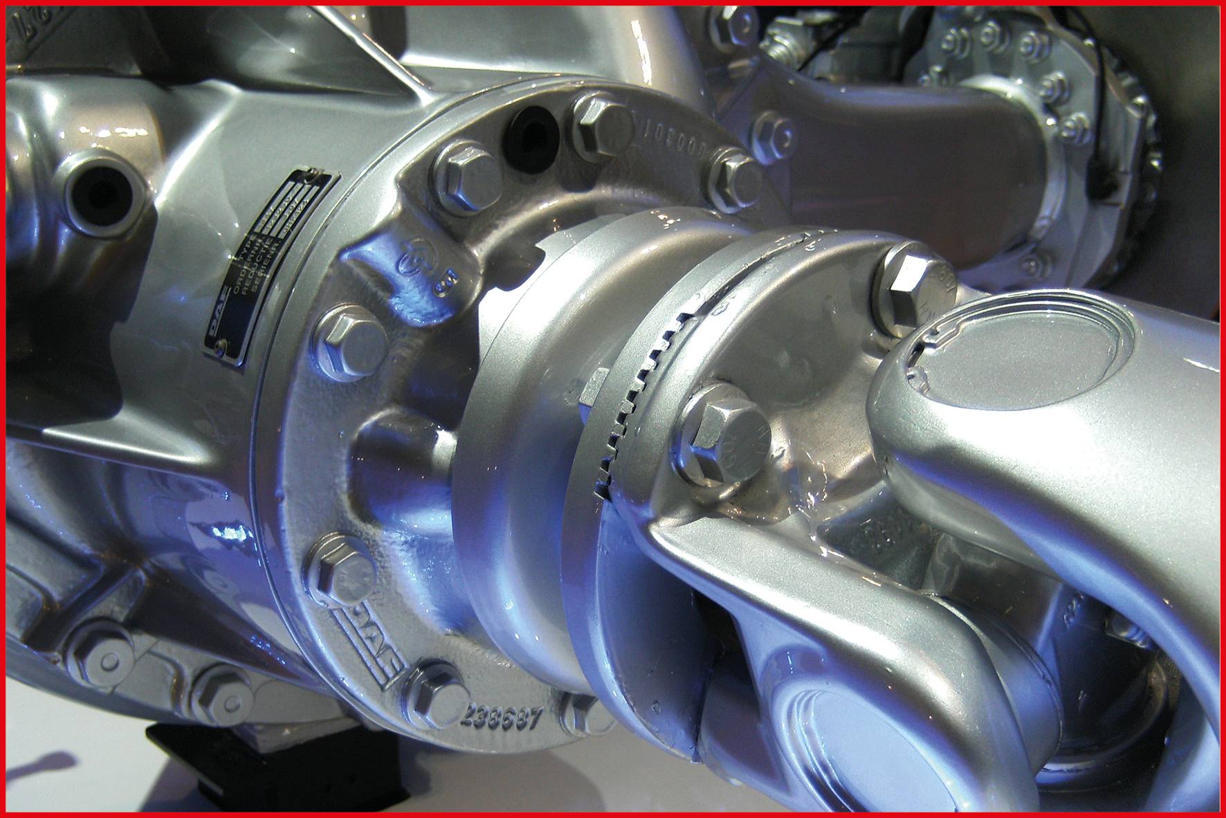 Zbliżenie błyszczącego elementu mechanicznego ze śrubami i przegubami, prawdopodobnie fragment silnika lub maszyny.