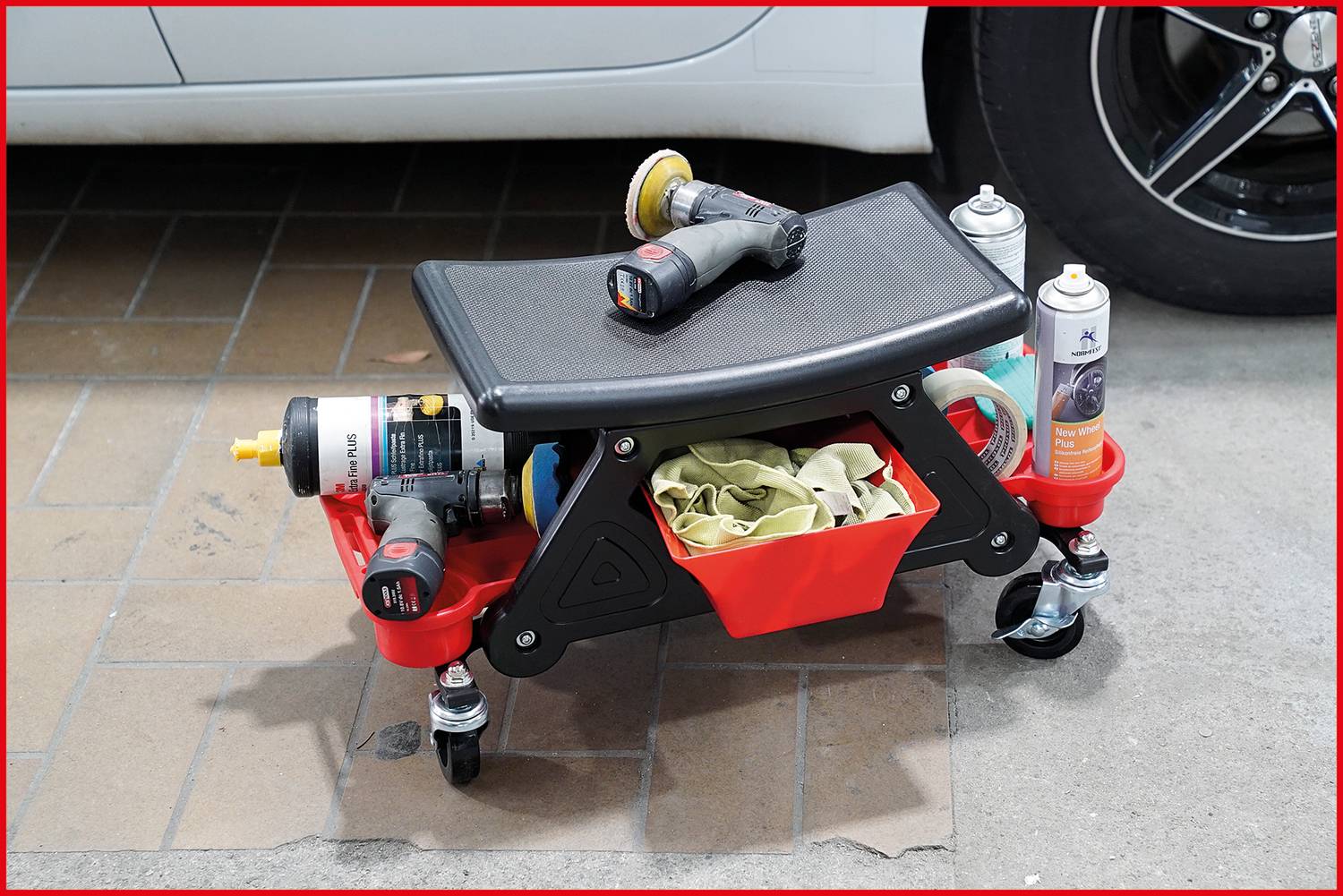 Mobilny wózek warsztatowy z siedziskiem jest wyposażony w maszynę polerską, środki czyszczące i ściereczki, stojący obok samochodu.