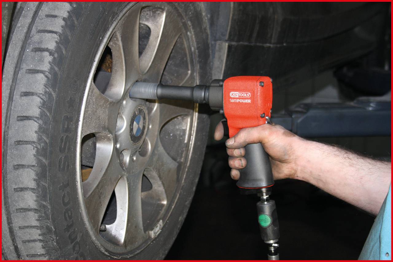 Osoba dokręca śruby koła samochodu wkrętarką pneumatyczną.