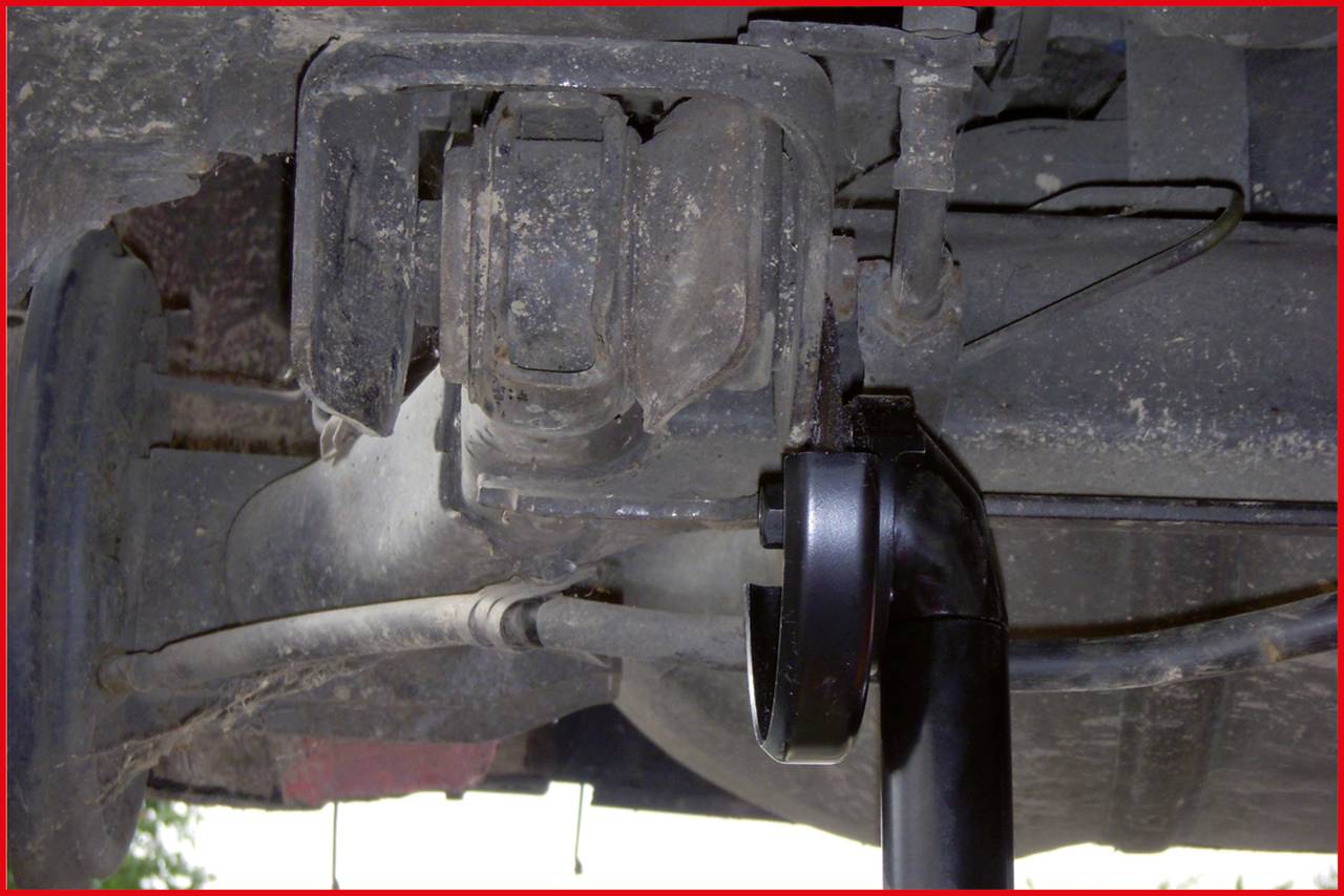 Zbliżenie podwozia samochodu, ukazujące elementy zawieszenia i element podpierający. Widoczne są wyraźne ślady zużycia i zabrudzenia.